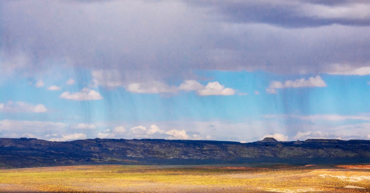 A scenic view of a vast field under a rainy sky in Page, Arizona, highlighting dramatic weather.
