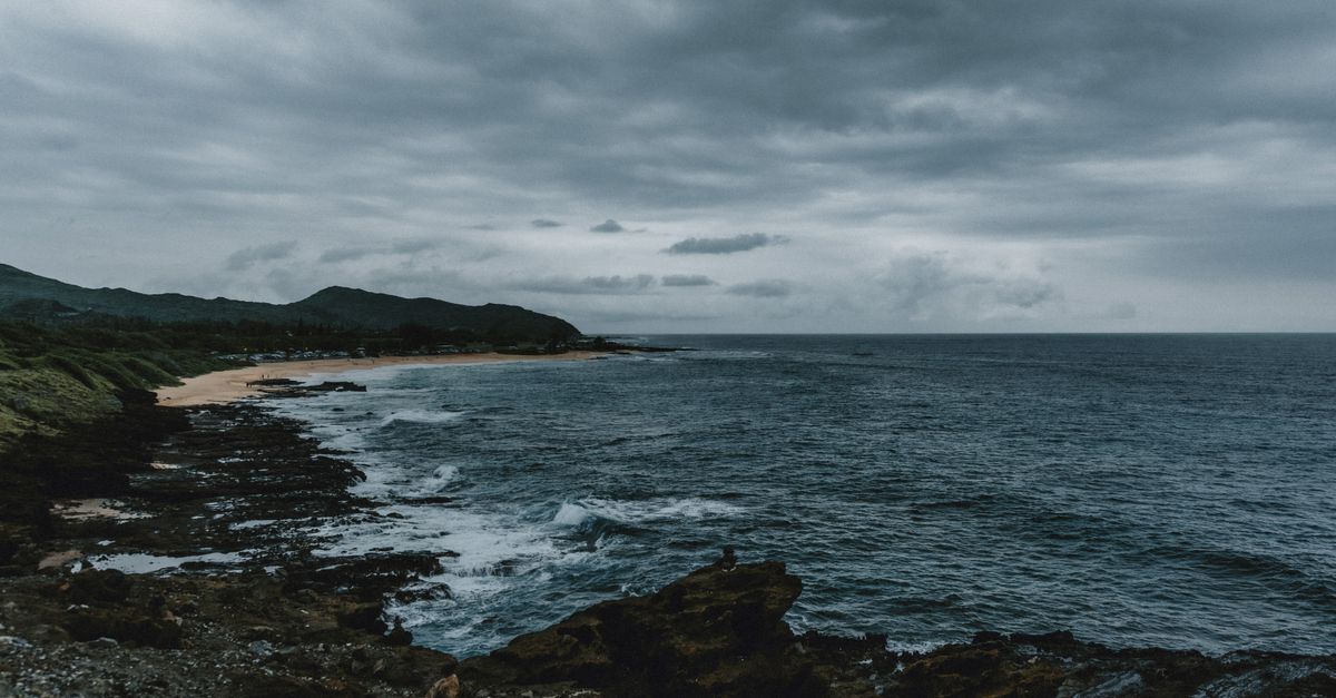 A dramatic view of Hawaiian coastline with storm clouds and rugged rocks.
