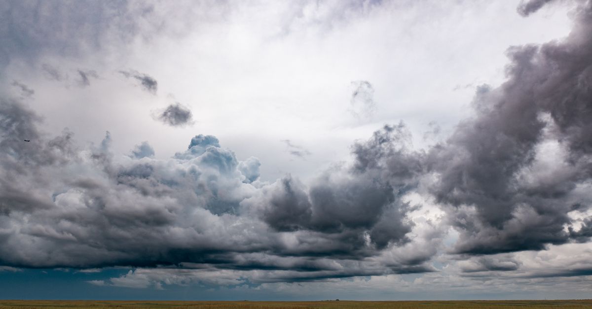 A breathtaking view of dark storm clouds looming over a vast green grassland in Miami, Florida.