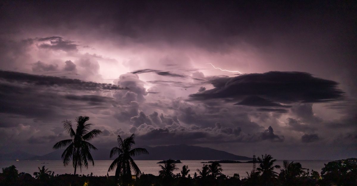 A striking view of lightning illuminating dark clouds above a tropical ocean landscape.