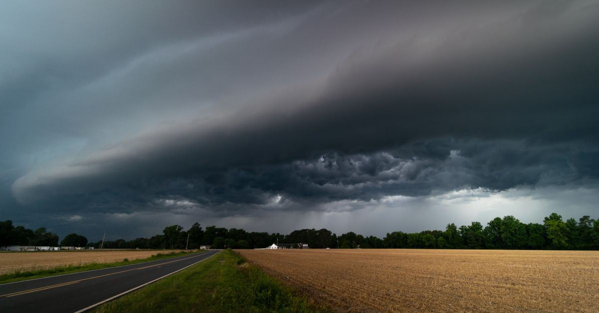 A mesmerizing view of dark storm clouds approaching over a rural road and farmland.