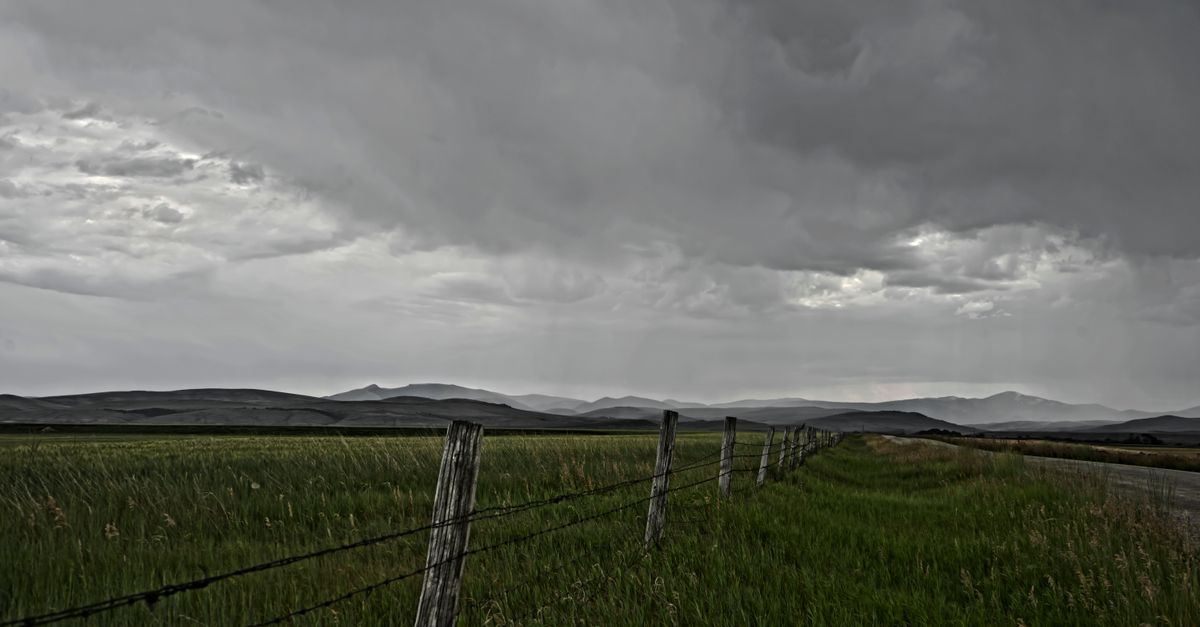 A moody, overcast day over a rural Montana landscape with barbed wire fence and mountains.