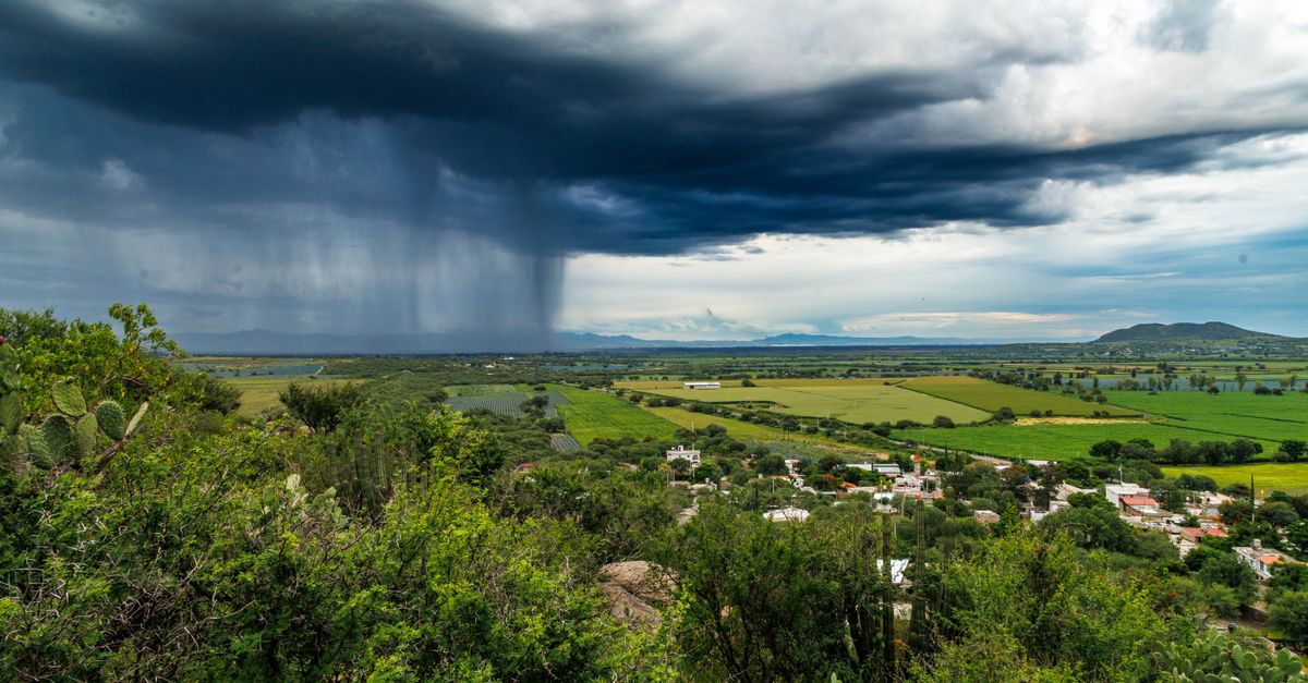 Dark storm clouds and heavy rain over lush green fields, creating a dramatic landscape scene.