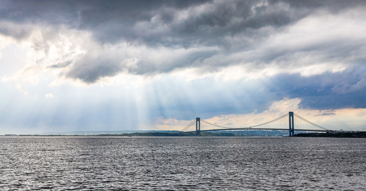 A dramatic sky with sun rays illuminating a bridge over a calm waterway, creating an inspiring landscape scene.