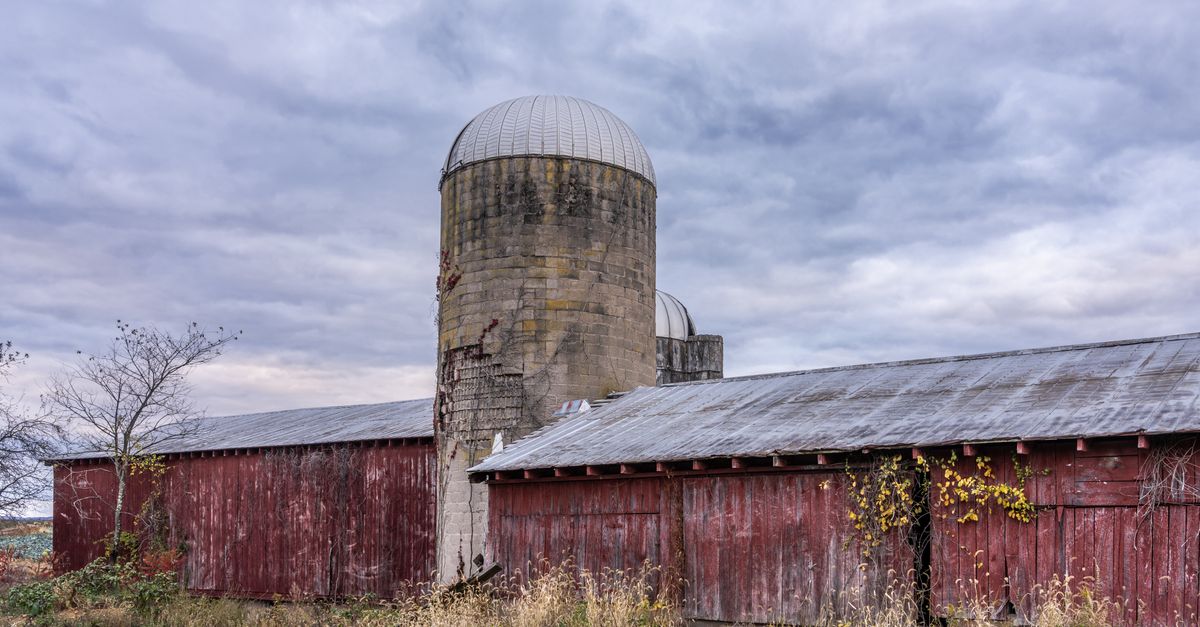 Weathered red barn and silo under cloudy skies in Muncy, Pennsylvania.