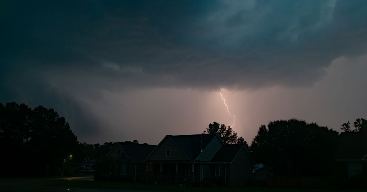 A striking lightning bolt illuminates suburban houses during a nighttime thunderstorm.